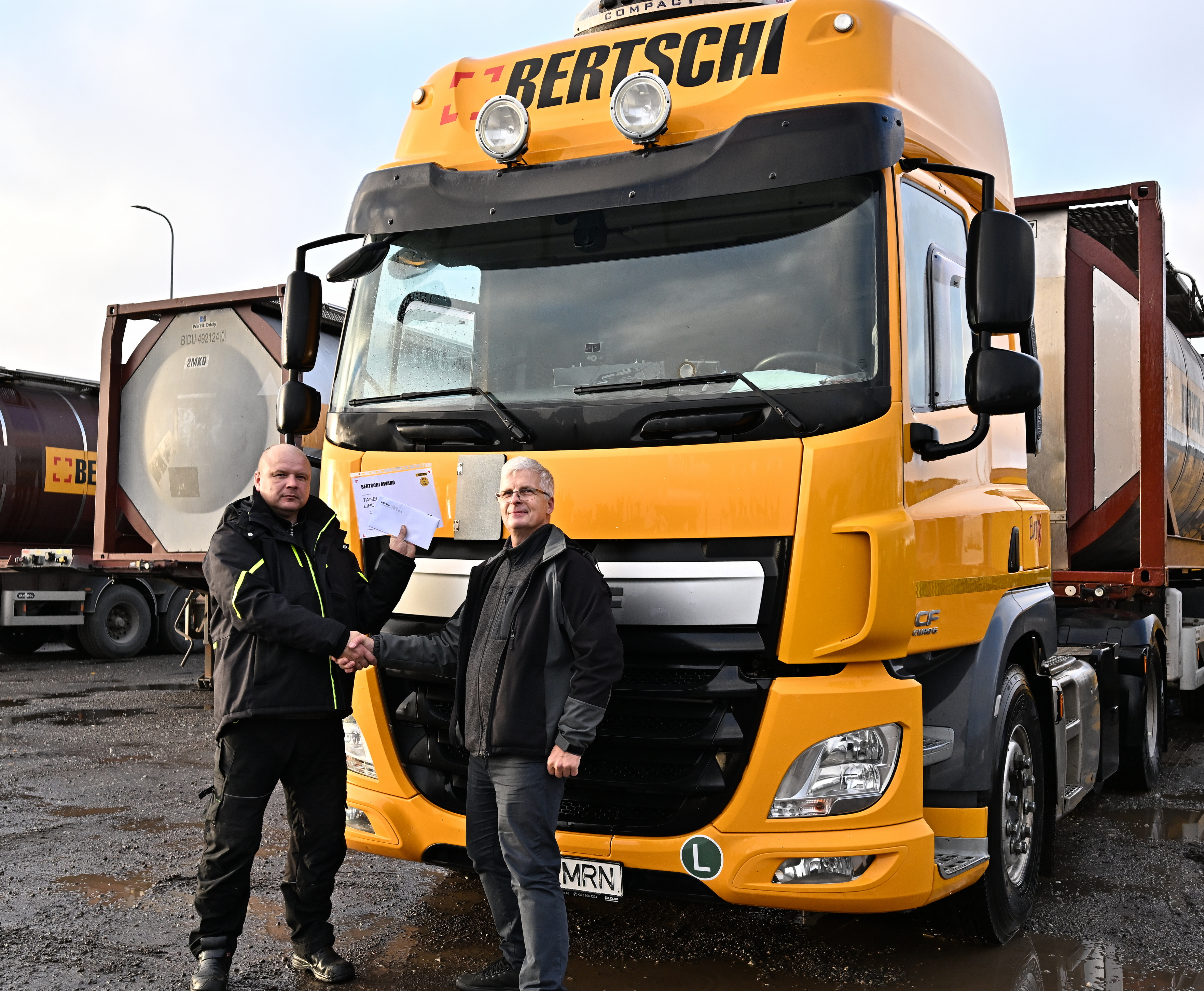 Two men posing in front of a Bertschi Truck. One is holding a paper that says Bertschi Award.