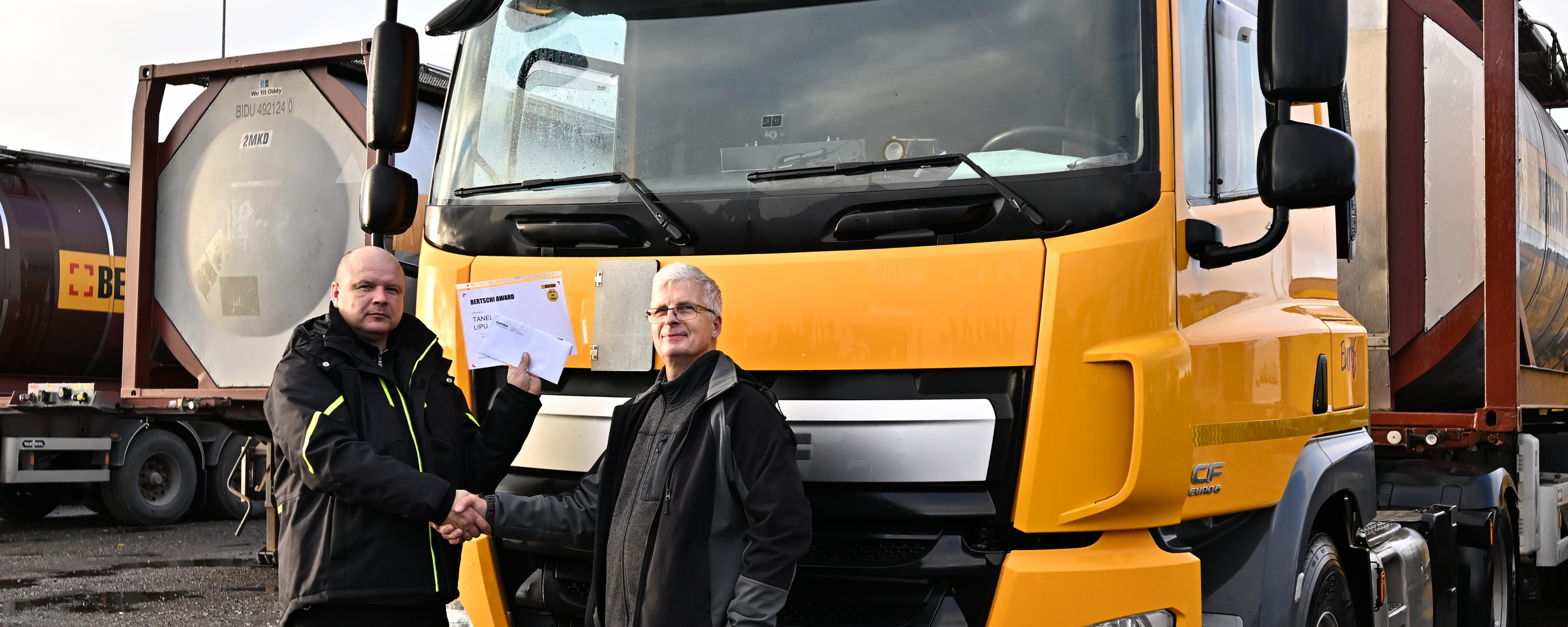 Two men posing in front of a Bertschi Truck. One is holding a paper that says Bertschi Award.