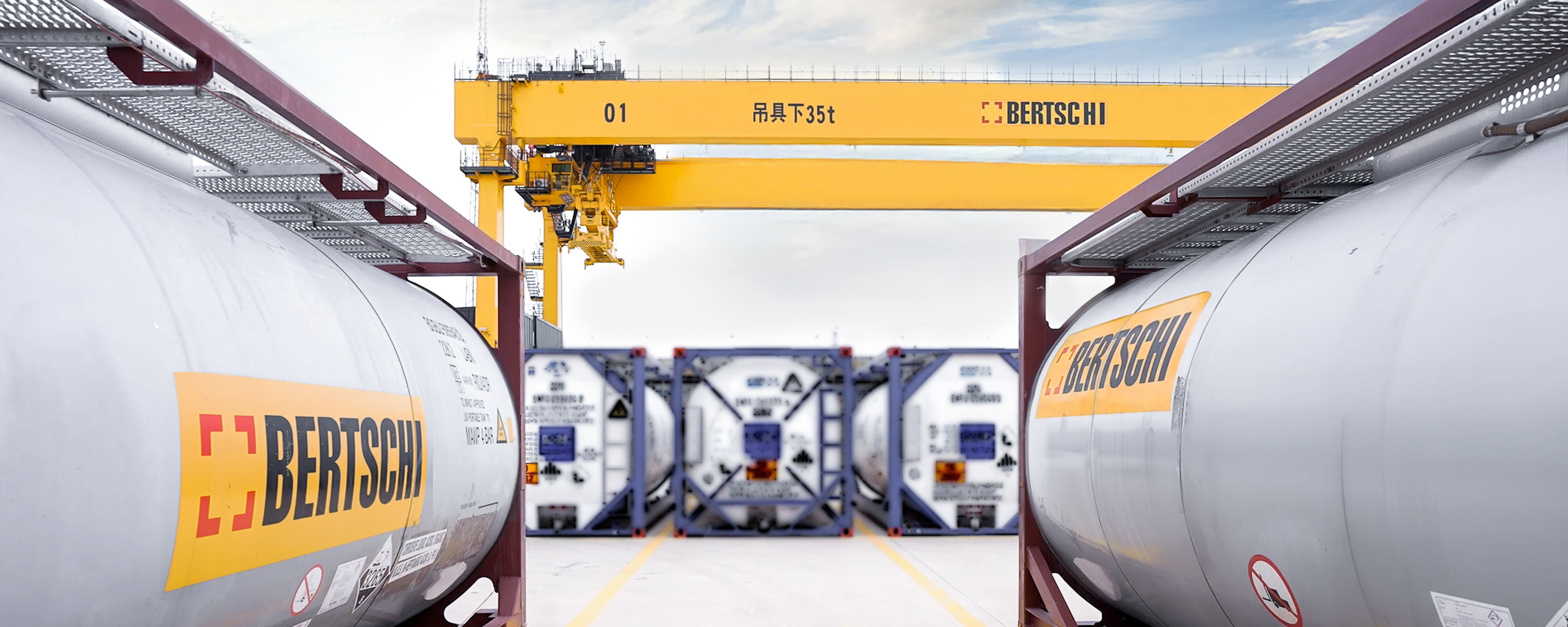 two bertschi isotanks facing a big yellow gantry crane